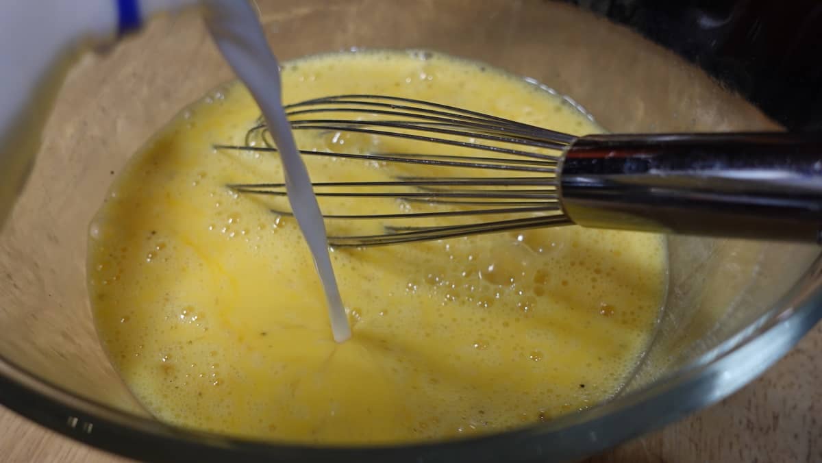 Milk being poured into a bowl with whisked eggs to make a tater tot breakfast bake.