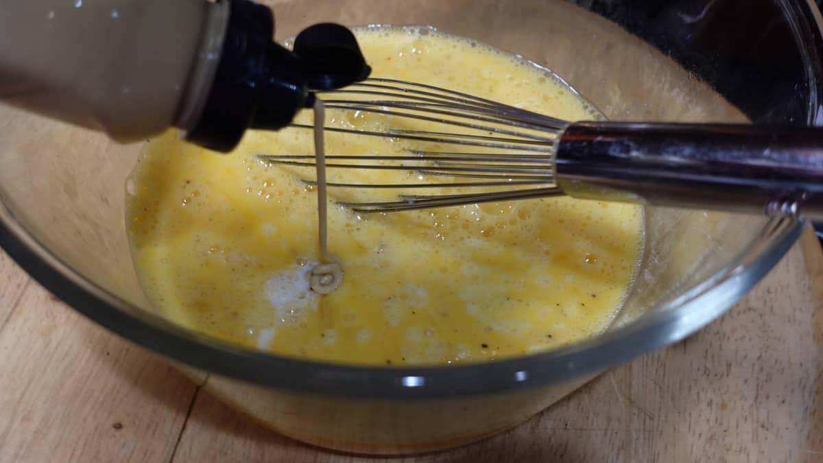 Dijon mustard being squirted into a bowl of scrambled eggs before cooking.