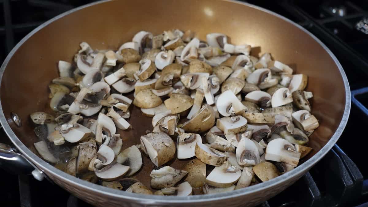 Sliced and quartered mushrooms in a skillet.