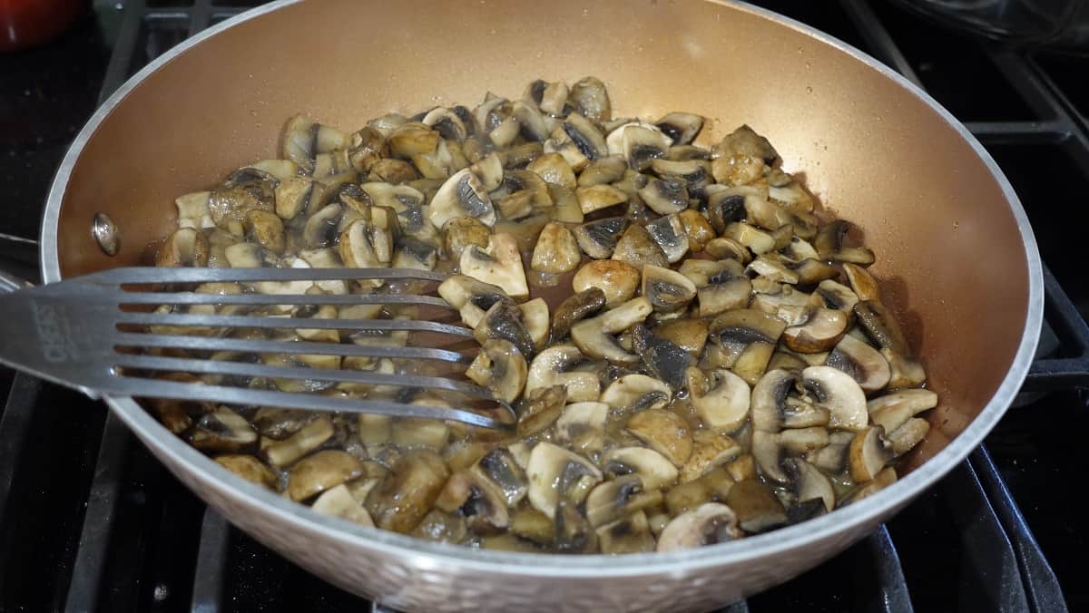 Sauteed mushrooms in a skillet along with a slotted spatula.