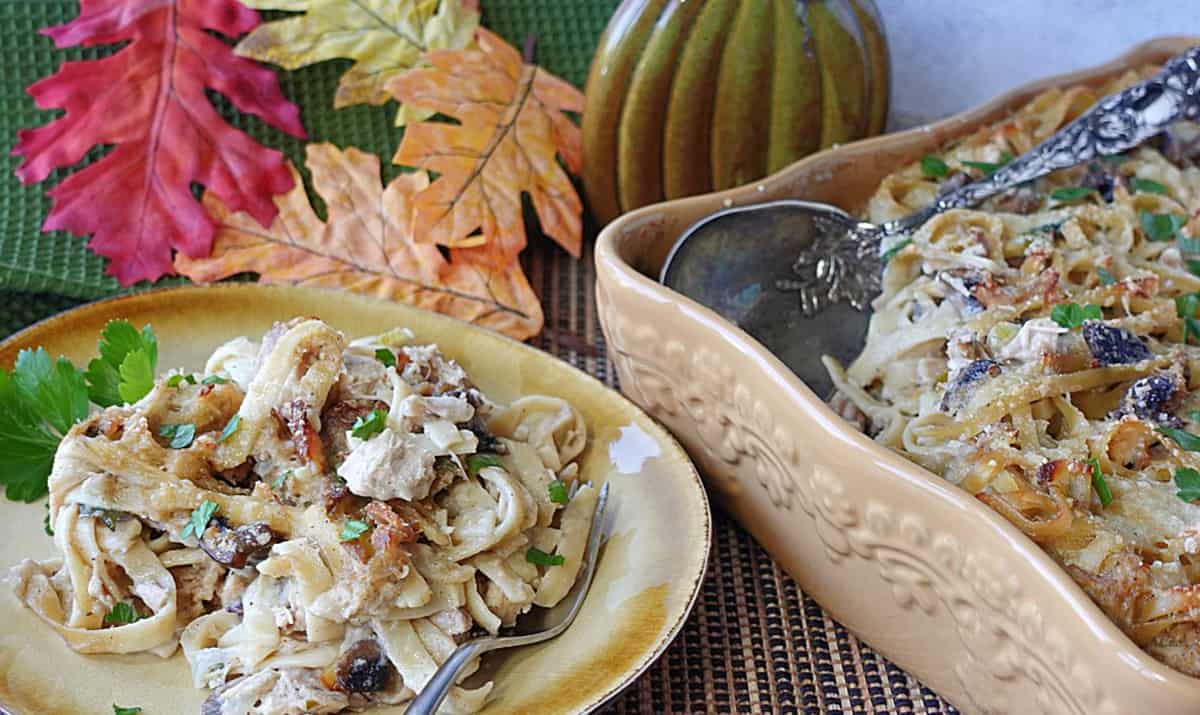 A serving of Turkey Tetrazzini with linguine on a plate along with a casserole dish on the side.