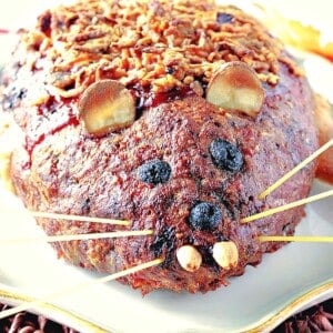 A closeup of a meatloaf shaped like a rat with almond teeth and spaghetti whiskers.