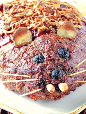 A closeup of a meatloaf shaped like a rat with almond teeth and spaghetti whiskers.