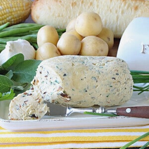 A butter knife and garlic and herb butter on a butter dish.