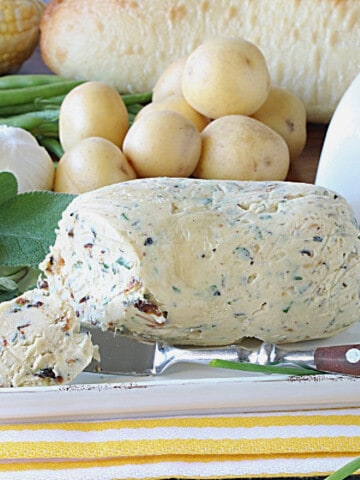 A butter knife and garlic and herb butter on a butter dish.