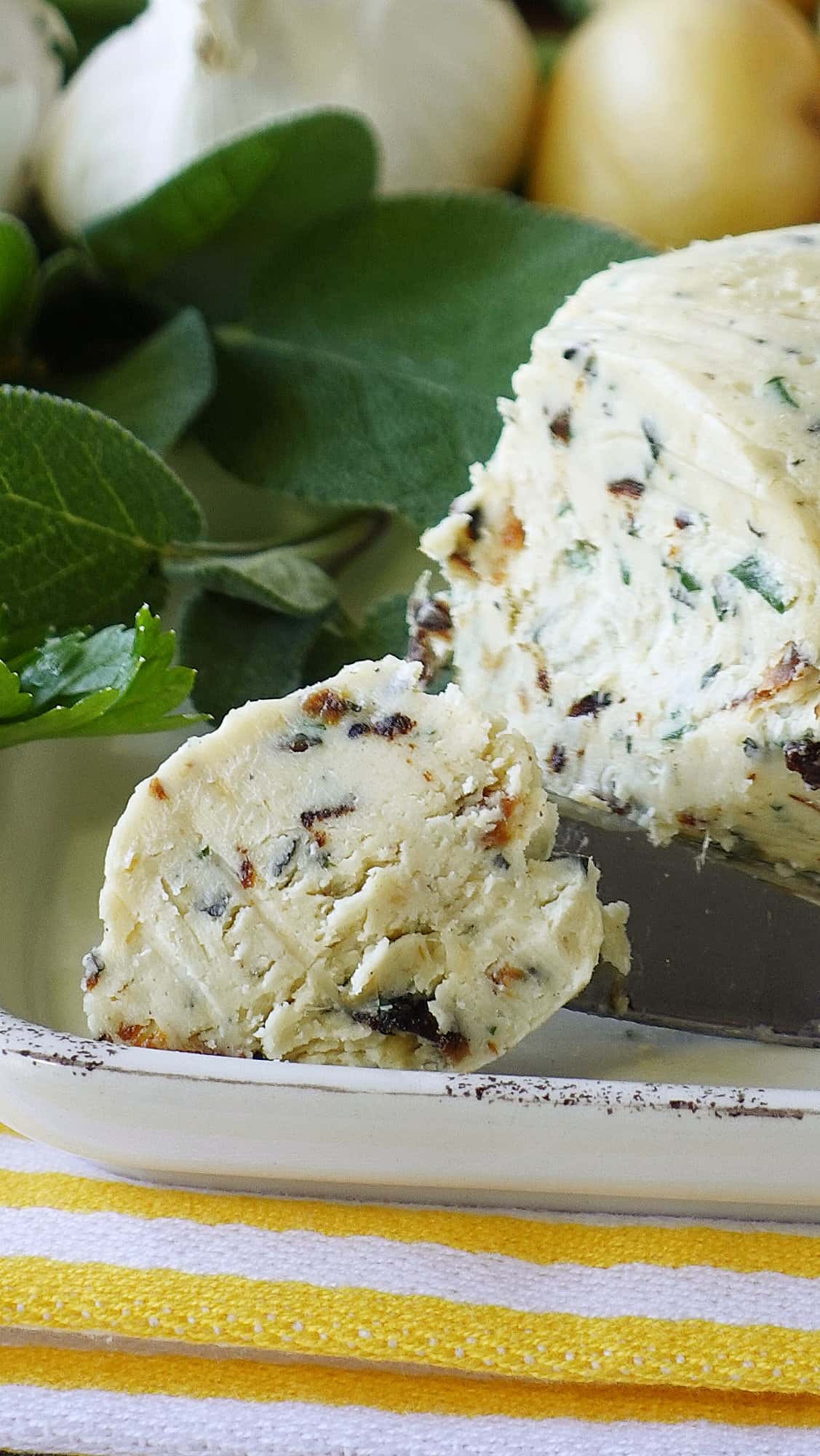 A log of Roasted Garlic Compound Butter with Herbs on a butter dish with herbs in the background.