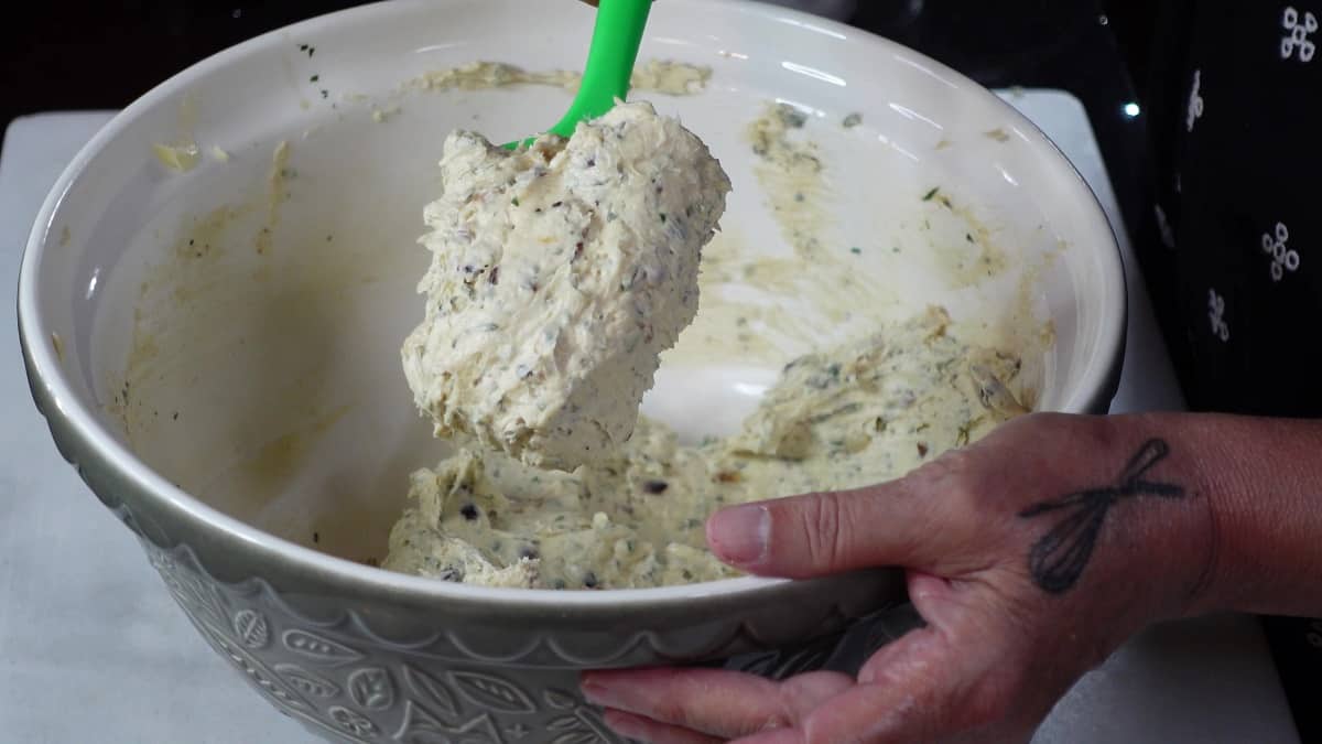 A green spatula holding a blob of homemade Roasted Garlic Compound Butter with Herbs.