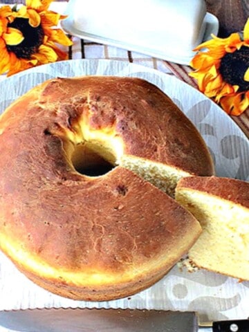 A round loaf of Sally Lunn Batter Bread on a plate with a serrated knife and a slice taken out.