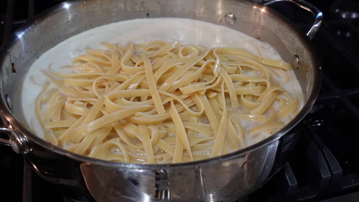 Cooked linguine added to a skillet with cream sauce.