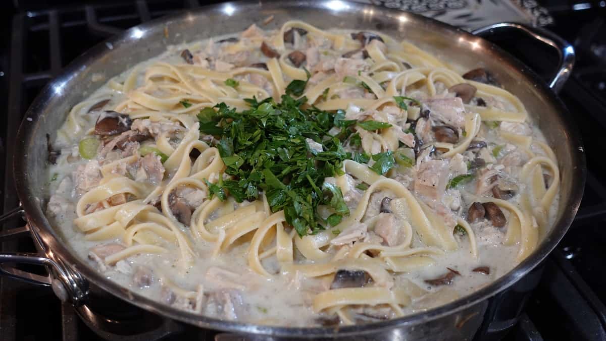 Fresh parsley added to a skillet with turkey tetrazzini.