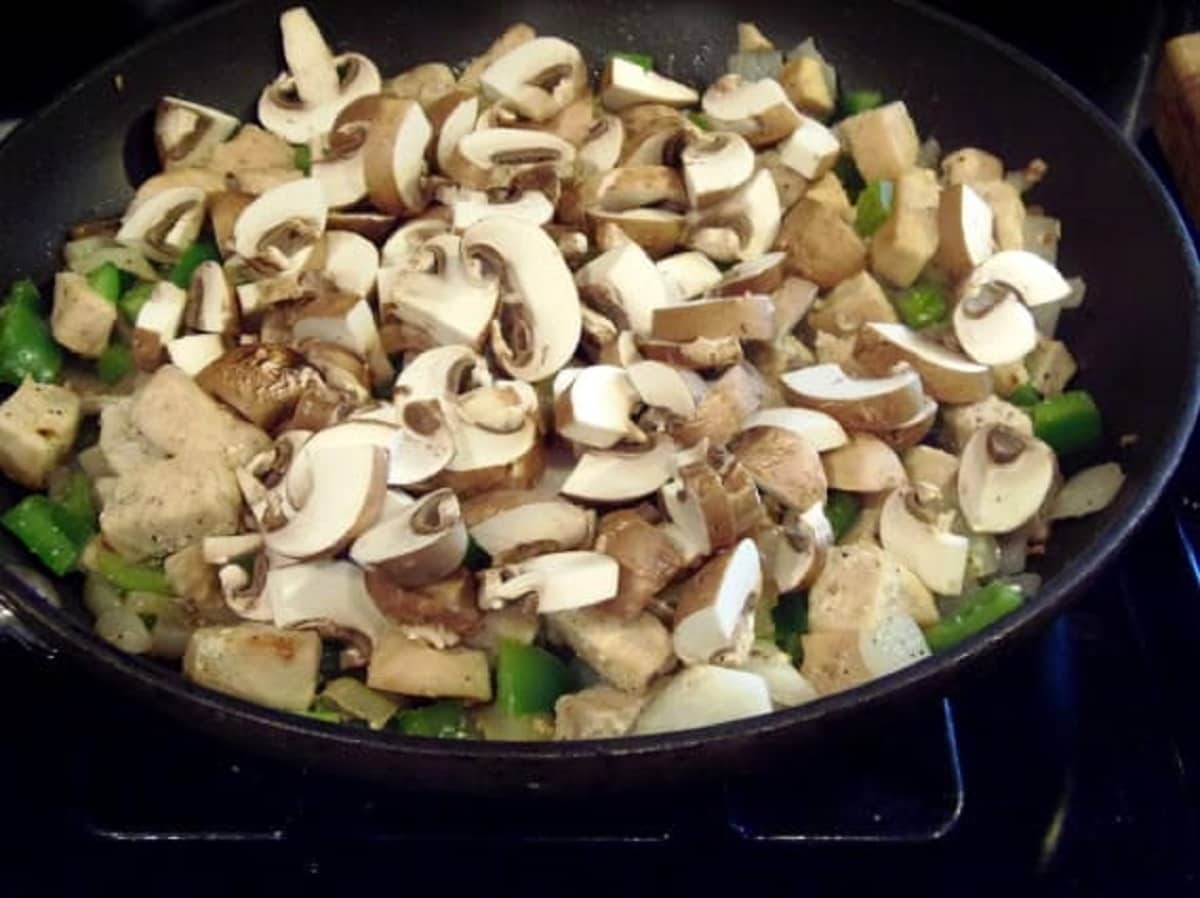 Chopped mushrooms in a skillet with green peppers and chicken.