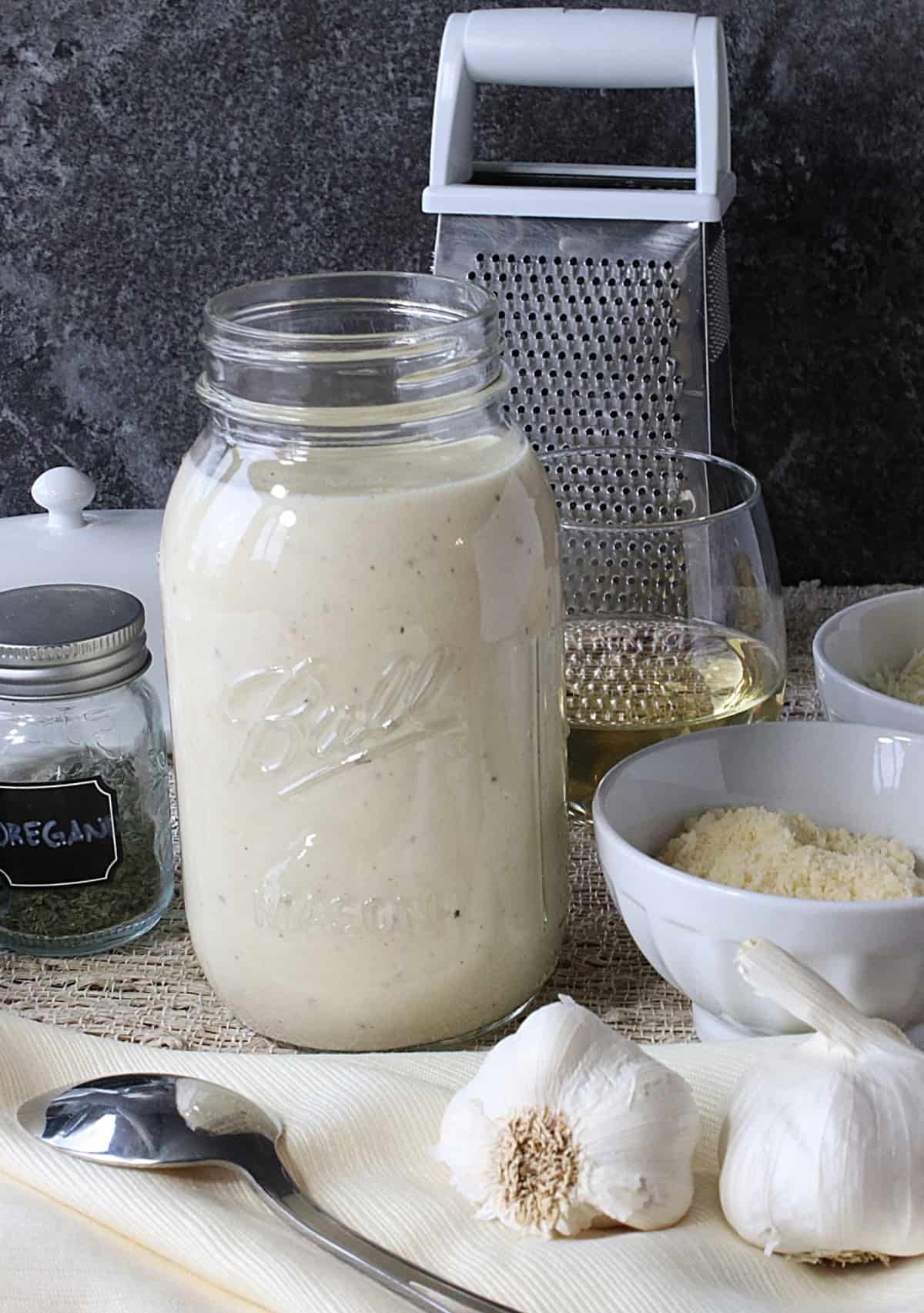 A jar filled with White Wine Alfredo Sauce with a wine glass and cheese grater in the background.