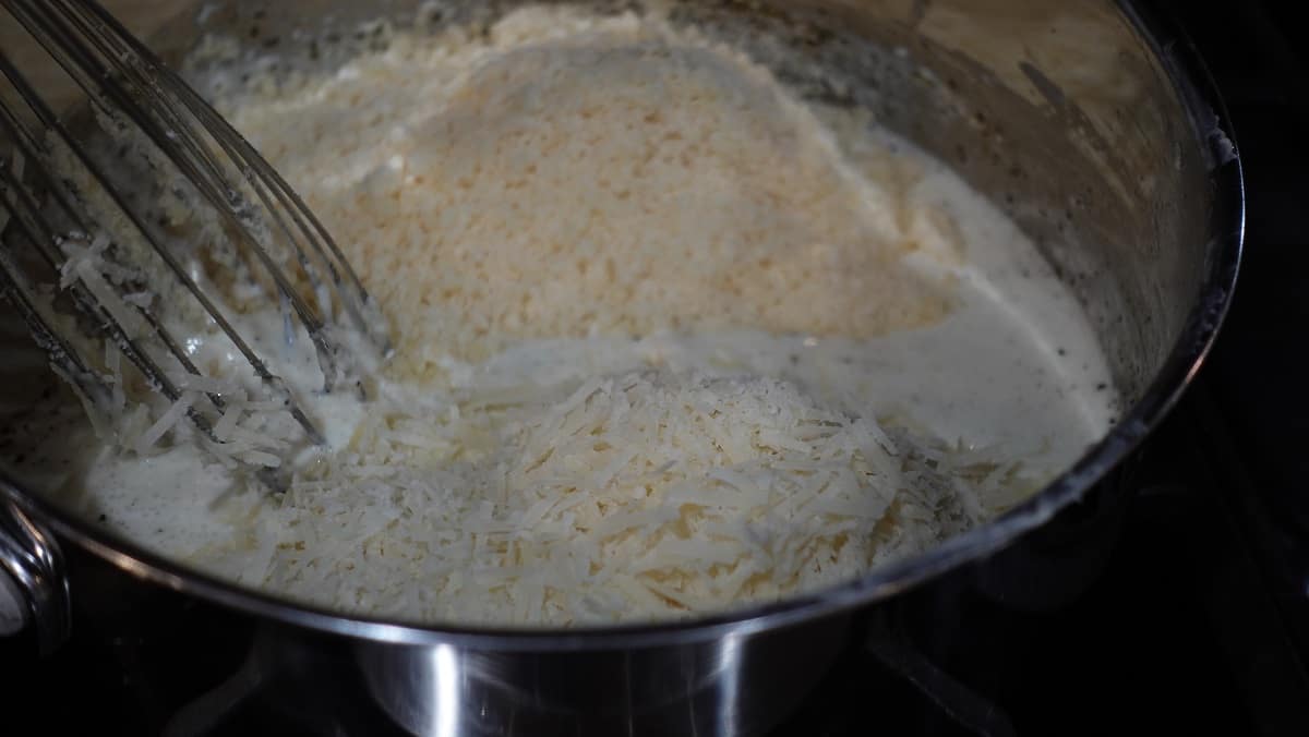Grated Parmesan and Romano cheese added to an Alfredo sauce with a whisk.