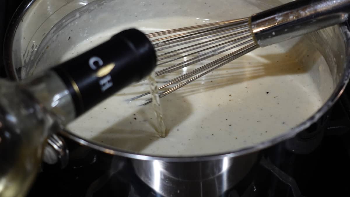 White wine being added to a Homemade White Wine Alfredo Sauce.