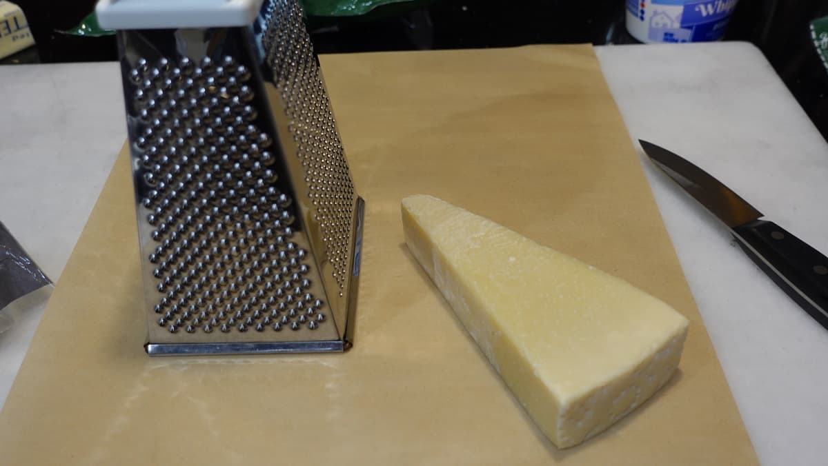 A wedge of Parmesan cheese and a box grater on a piece of parchment paper.