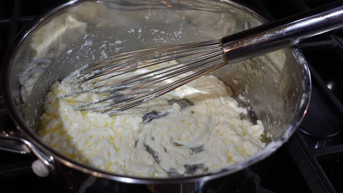 Cream cheese mixed with butter in a saucepan with a whisk.