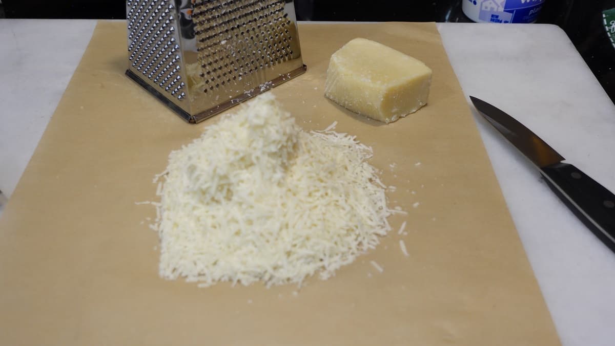 Grated Romano cheese on a piece of parchment paper and a box grater.