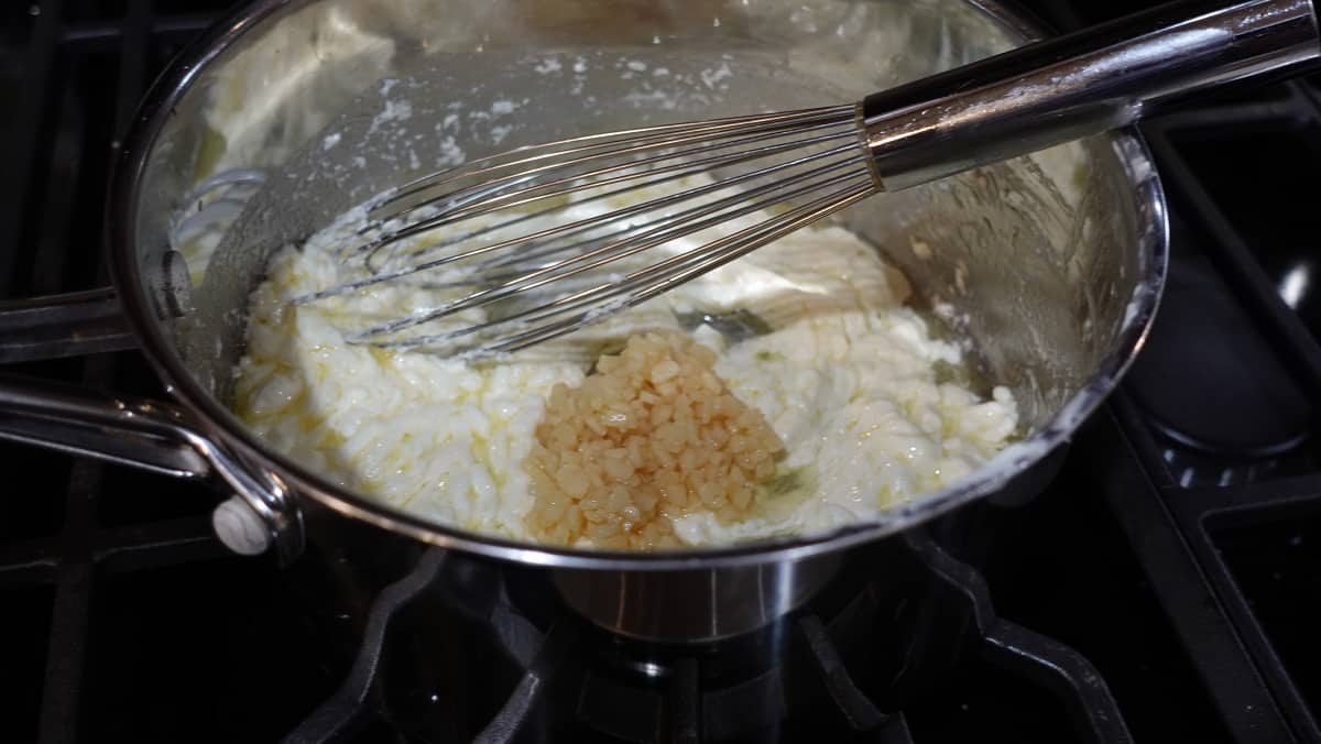 Minced garlic added to a cream cheese and butter mixture in a saucepan.