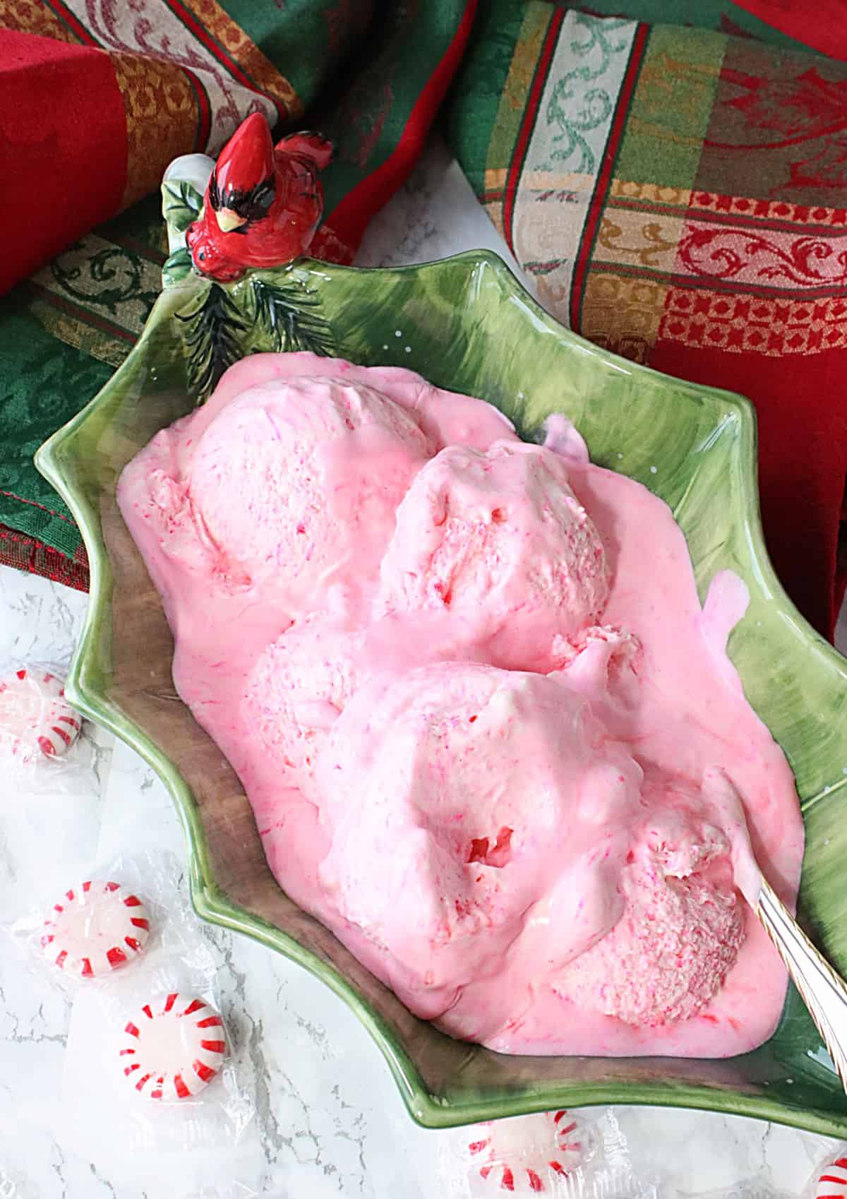 A green holly berry bowl filled with scoops of melting pink Peppermint Schnapps Ice Cream.