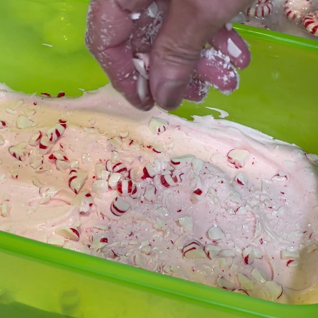 Crushed peppermint candy being put on top of ice cream.
