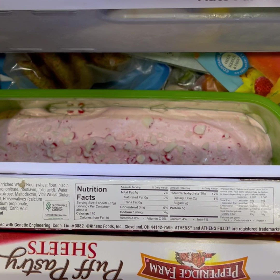 A container of pink peppermint ice cream being put into a freezer.