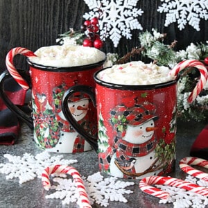 Two mugs filled with Peppermint White Hot Chocolate with candy canes and snowflakes.