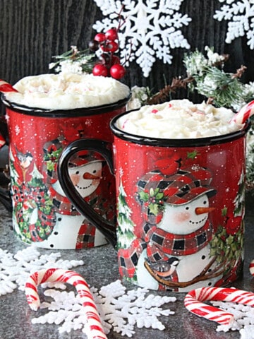 Two mugs filled with Peppermint White Hot Chocolate with candy canes and snowflakes.