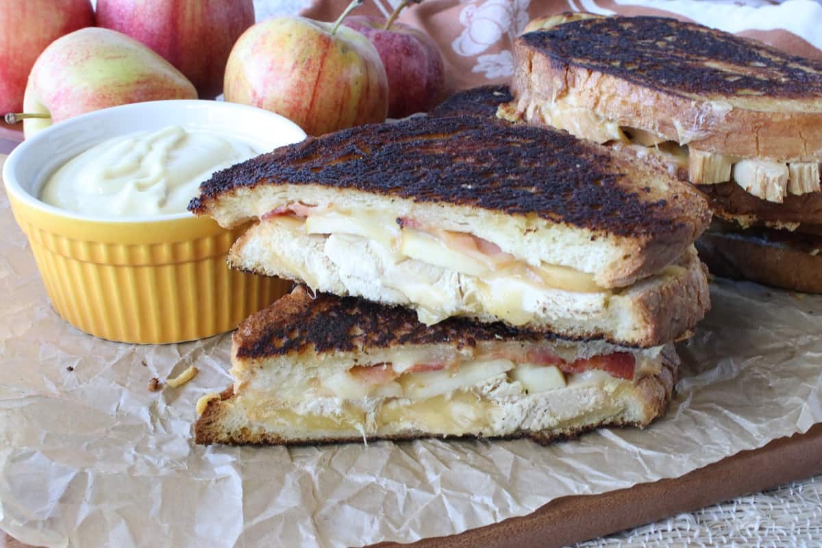 A grilled cheese with turkey sandwich and apples in the background.
