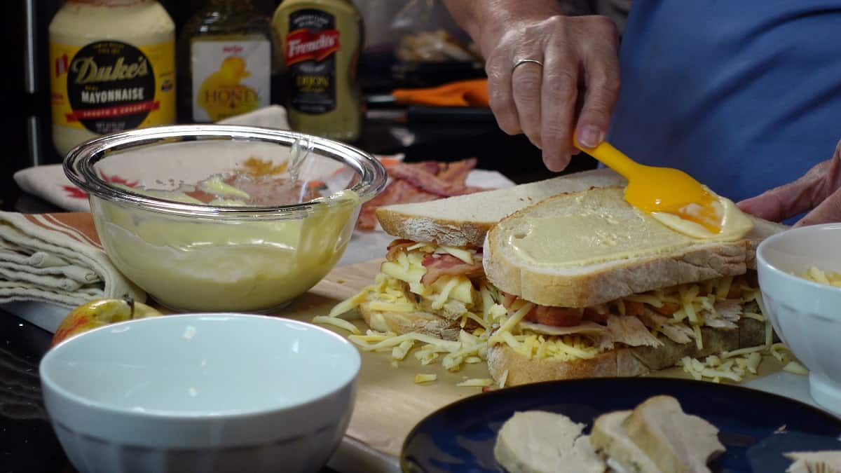 Mayo mustard being spread on the bread of a sandwich.