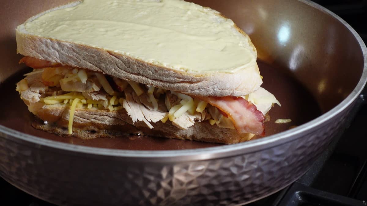 A grilled cheese sandwich with turkey and bacon in a skillet.