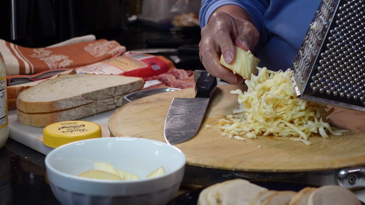 A block of Gouda cheese being grated on a box grater.