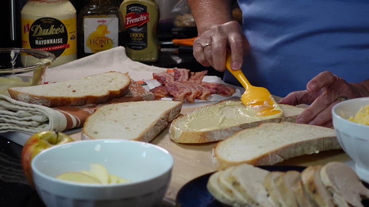 Mustard mayo being added to bread with a spatula.