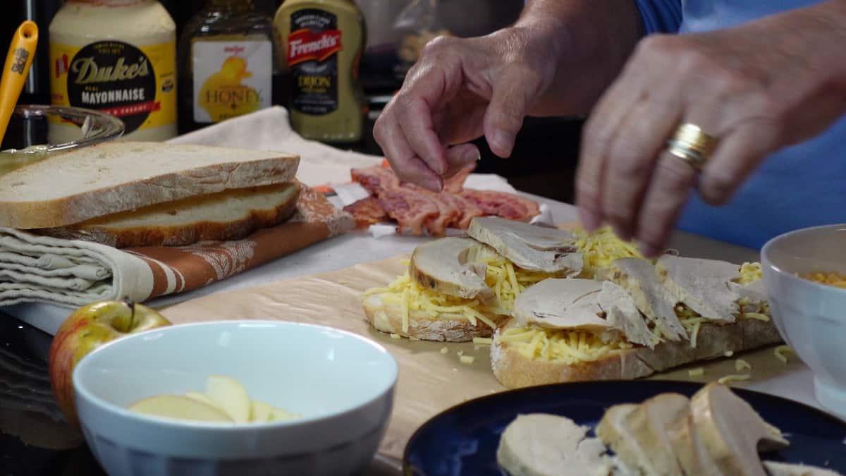 Leftover turkey slices being added to a grilled cheese sandwich before cooking.