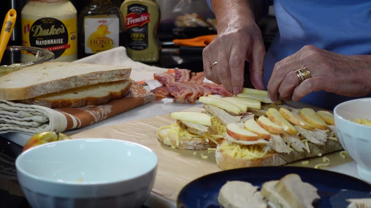 Apple slices being added to a sandwich for grilling.