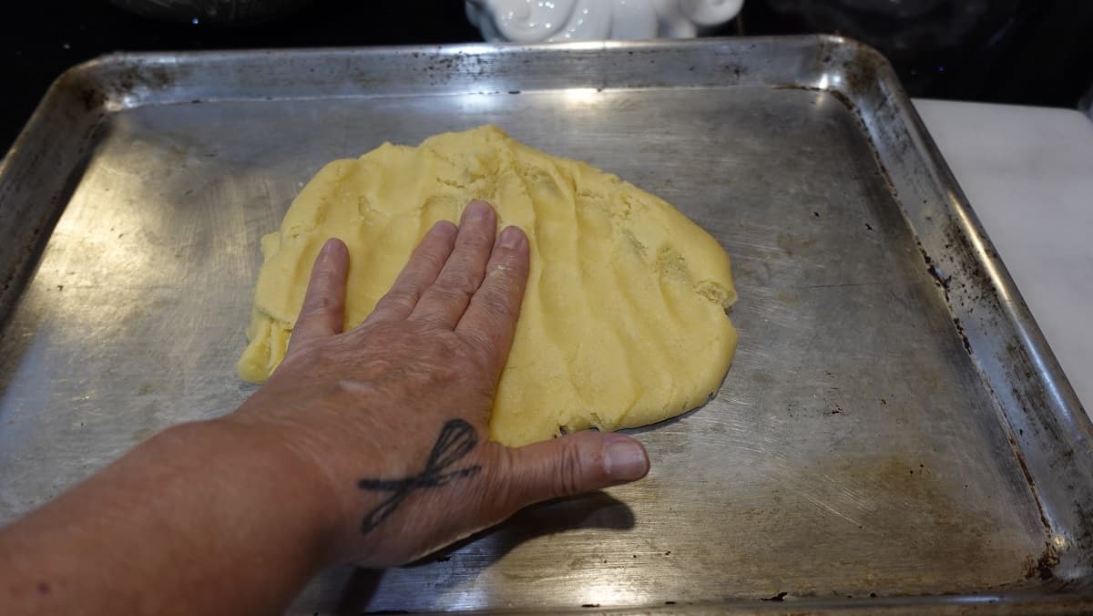 Dough being pressed out on a baking sheet.