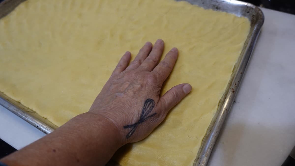 A hand spreading out cookie dough on a baking sheet.