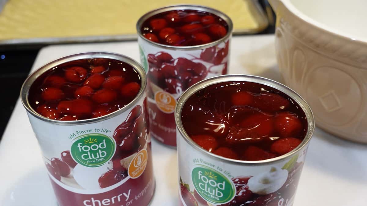 Three open cans of cherry pie filling on a counter.