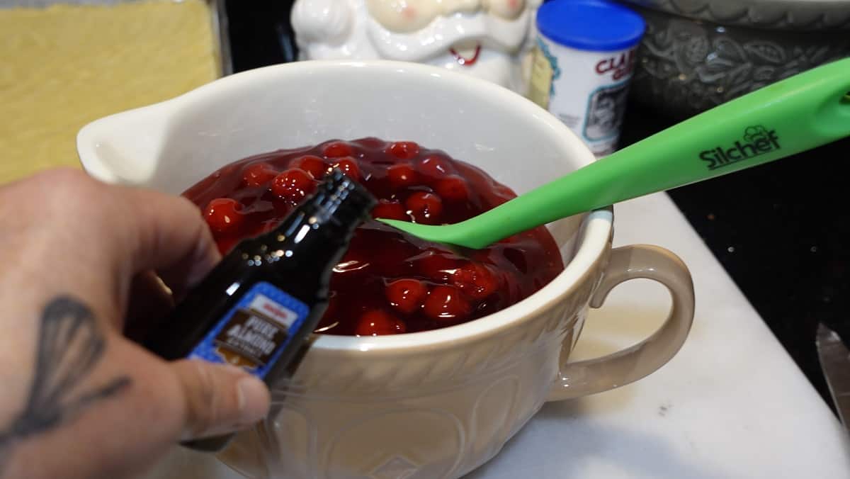 Almond extract being added to a bowl of cherry pie filling.
