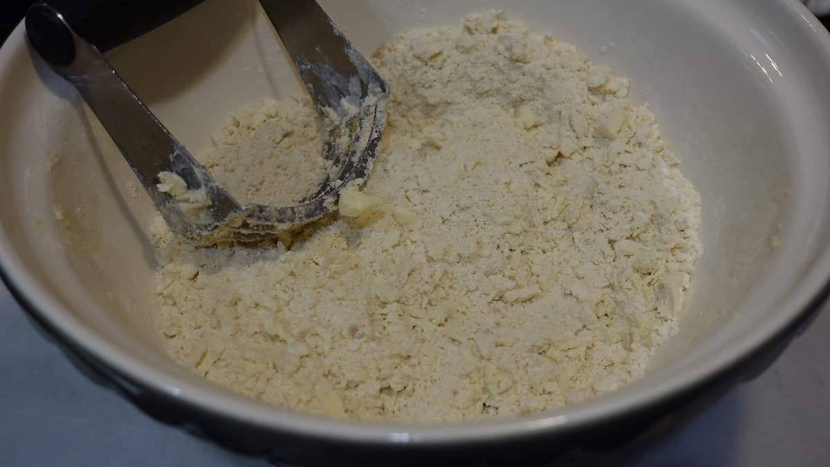 A crumb topping being made in a bowl with a pastry cutter.