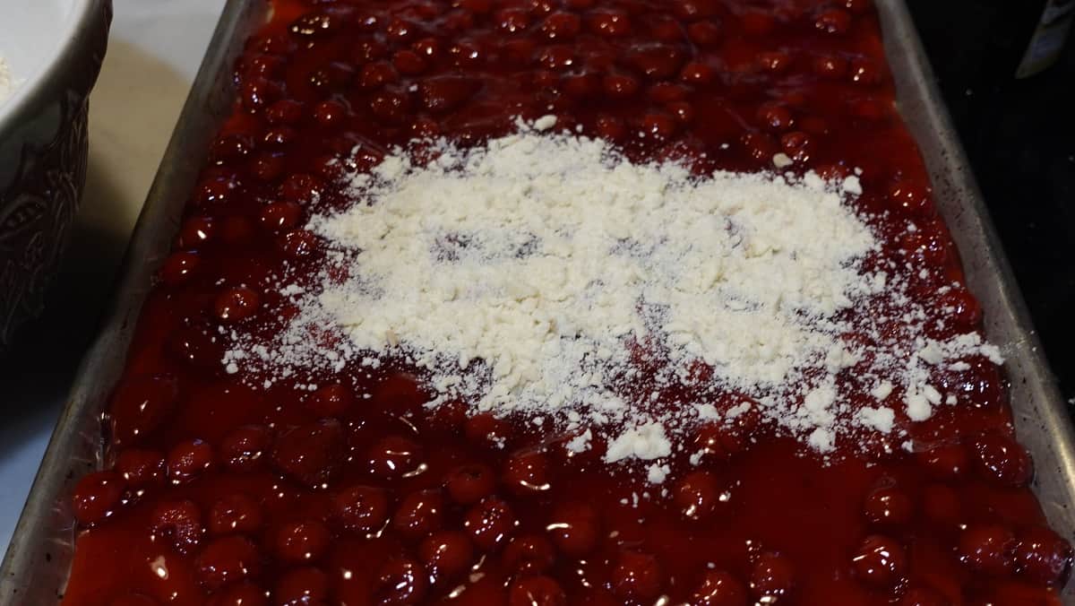 A crumb topping starting to be spread on top of cherry filling.