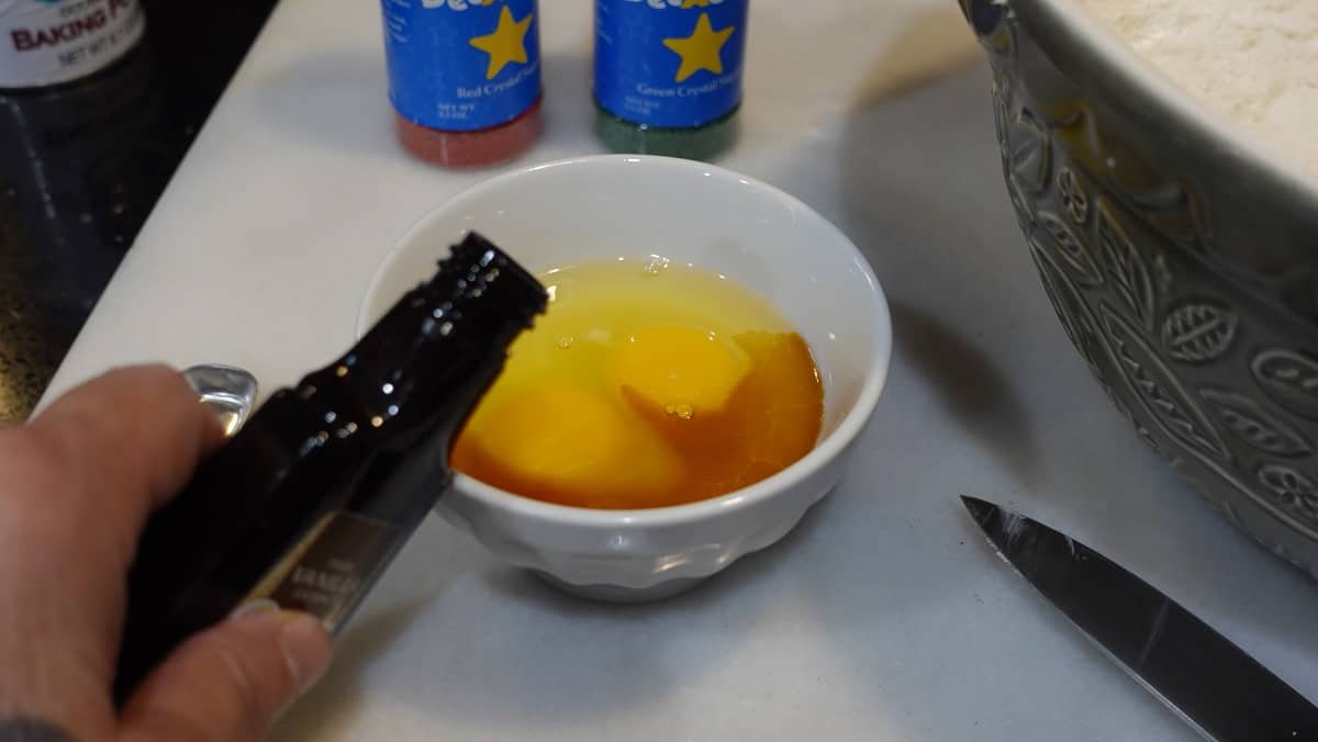 Vanilla extract being poured into a small bowl of eggs.