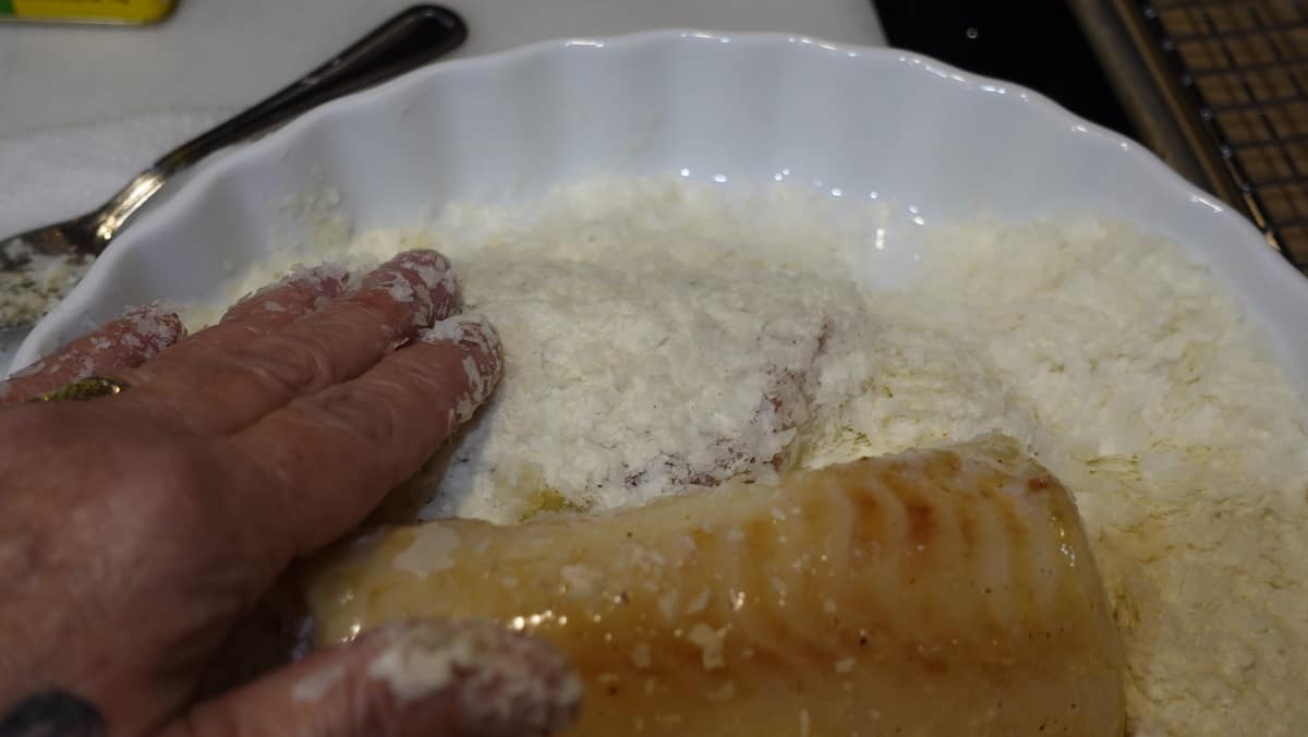 Cod fillets being coated with instant mashed potato flakes.