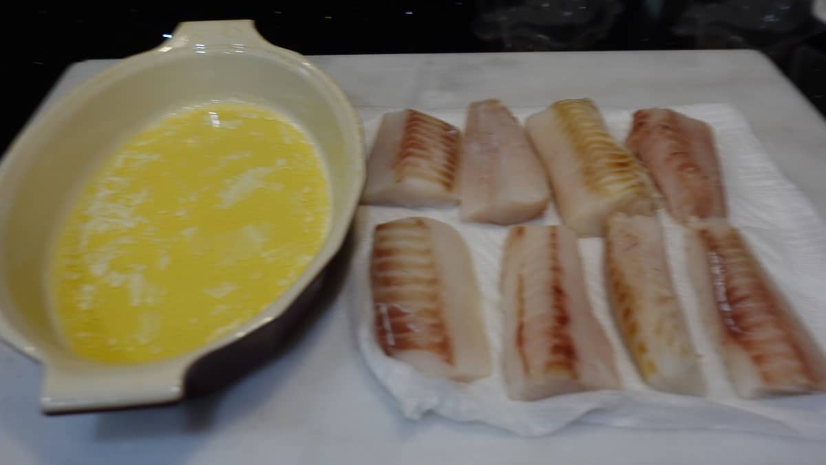 Cod fillets on paper towels along with a shallow dish with melted butter.