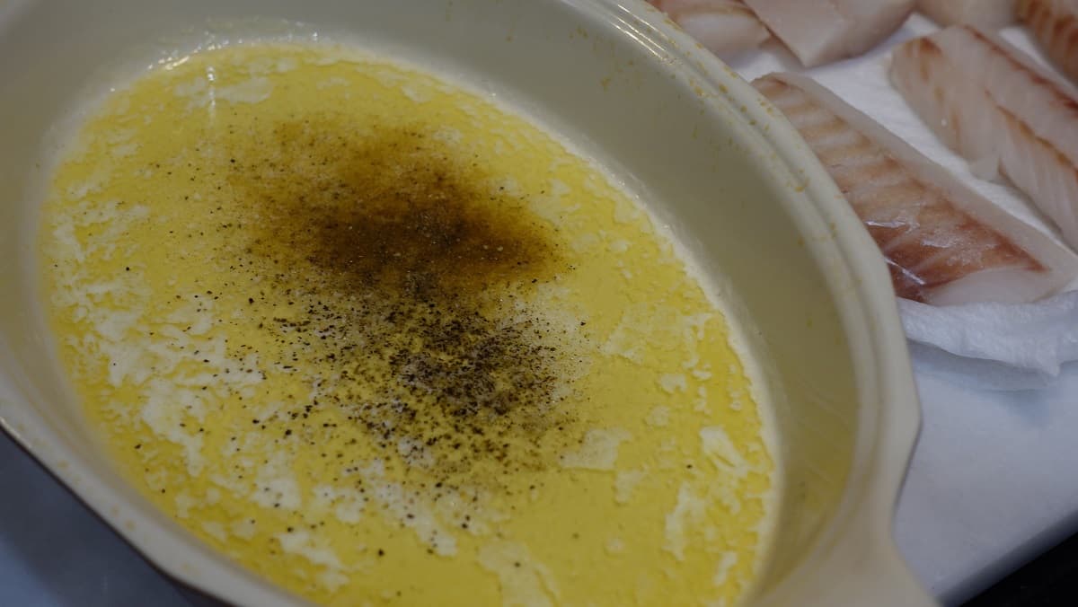 Melted butter in a shallow dish with seasonings.