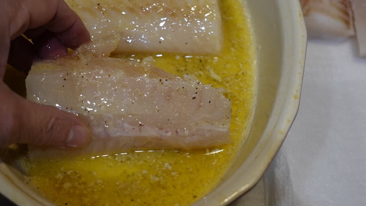 Cod fillets being dipped in melted butter.
