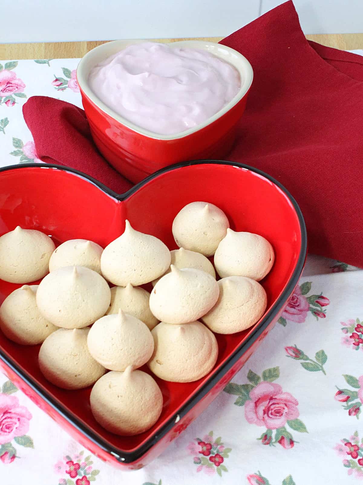 A heart-shaped red bowl filled with Almond Meringue Cookies.