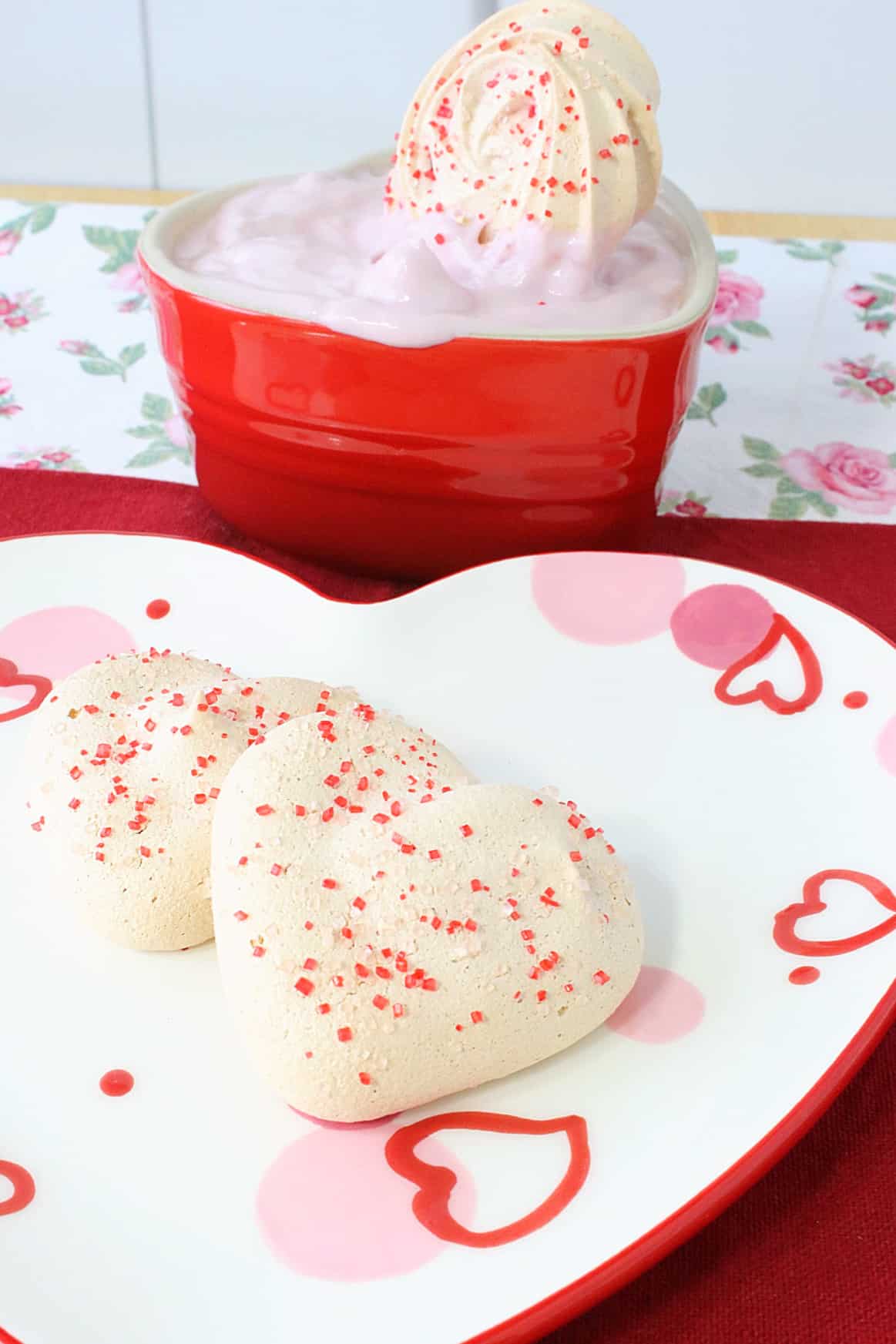 Two heart-shaped Almond Meringue Cookies on a Valentine's Day plate.