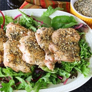 Baked chicken thighs on a platter with greens underneath and everything seasoning on the chicken.