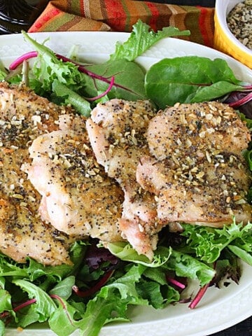 Baked chicken thighs on a platter with greens underneath and everything seasoning on the chicken.