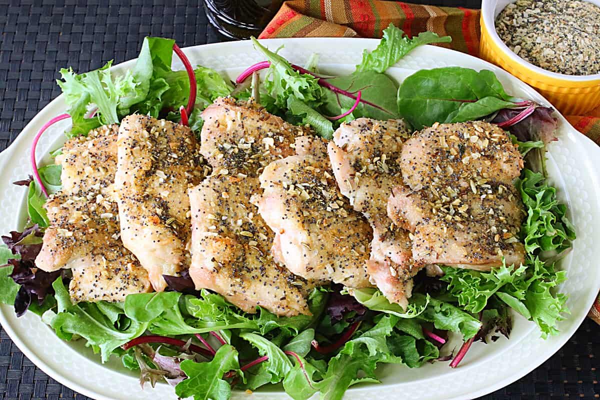 Six baked chicken thighs on an oval platter with salad green as the base.